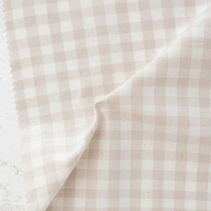 May include: A piece of beige and white gingham fabric. The fabric is folded, showing the texture and pattern of the woven material. The word "FABLEISM" is printed in the bottom right corner.