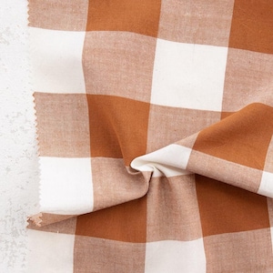May include: Close-up of a fabric sample with a large brown and white checkered pattern. The fabric is folded, showing the texture and weave. The edge of the fabric is unfinished, revealing the raw edge. The word "FABLEISH" is printed on the fabric.
