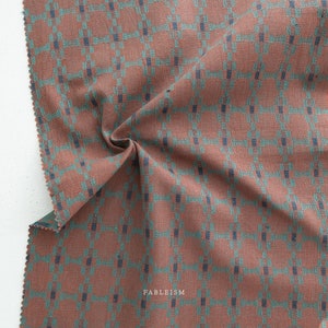 May include: Close-up of a folded fabric with a plaid pattern. The fabric is primarily a reddish-brown color, with a grid of teal and navy blue lines. The word "FABLEISM" is printed in white at the bottom right.