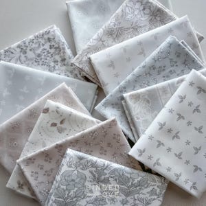 Peut inclure: Un assortiment de carr&eacute;s de tissu pli&eacute;s dans diverses nuances de gris, blanc et beige. Les tissus pr&eacute;sentent des motifs floraux et botaniques, notamment des feuilles, des fleurs et des vignes. Certains carr&eacute;s sont unis, d'autres pr&eacute;sentent des motifs complexes.