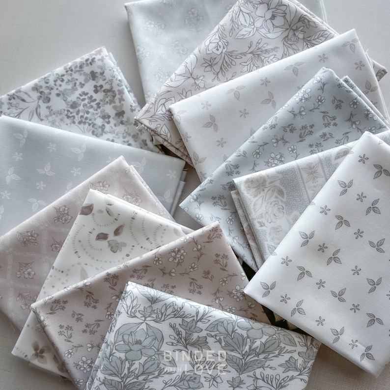 Peut inclure: Un assortiment de carr&eacute;s de tissu pli&eacute;s dans diverses nuances de gris, blanc et beige. Les tissus pr&eacute;sentent des motifs floraux et botaniques, notamment des feuilles, des fleurs et des vignes. Certains carr&eacute;s sont unis, d'autres pr&eacute;sentent des motifs complexes.