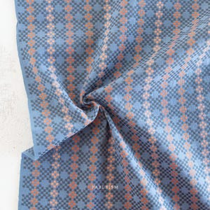 May include: Close-up of a blue fabric with a geometric pattern in orange and gray. The fabric is folded, showing the texture and design. The word "FABLEISM" is printed on the fabric.