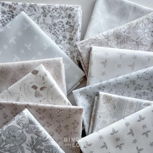 Peut inclure: Un assortiment de morceaux de tissu pli&eacute;s dans des tons de gris et de blanc. Les tissus pr&eacute;sentent des motifs floraux et de feuilles, certains affichant de petits motifs de fleurs et de feuilles. La phrase "BIND WITH LOVE" est visible sur l'un des morceaux de tissu.