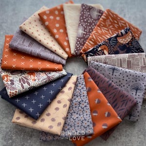 May include: A collection of folded fabric squares arranged in a circular fan pattern. The textiles feature various prints including floral, geometric, and woodland motifs in a color palette of burnt orange, navy blue, cream, and muted purple tones.