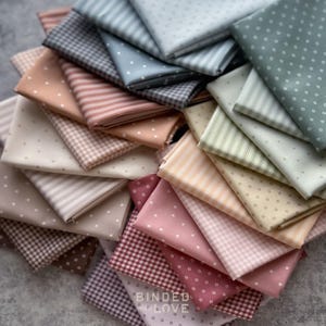 May include: A collection of folded fabric squares in various colors and patterns. The fabrics include polka dots, stripes, and gingham in shades of pink, blue, and neutral tones. The text "BINDED LOVE" is visible on one of the fabric squares.
