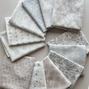 Peut inclure: Une collection de carr&eacute;s de tissu pli&eacute;s dans diverses nuances de gris et de blanc, avec des motifs floraux et g&eacute;om&eacute;triques. Les tissus sont dispos&eacute;s en cercle, mettant en valeur les diff&eacute;rents motifs. Le texte "BOUND WITH LOVE" est visible sur l'un des carr&eacute;s de tissu.