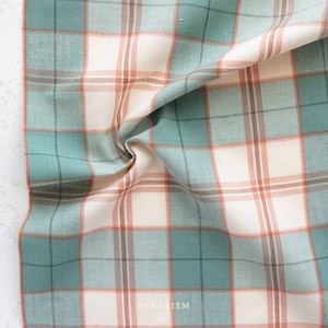 May include: A close-up of a fabric with a plaid pattern. The fabric features a grid of intersecting lines in shades of teal, cream, and rust. The fabric is slightly crumpled, with the word "FABLEISM" visible in the bottom right corner.