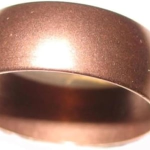 May include: A wide, copper-colored metal ring. The ring has a smooth, rounded exterior and a hollow interior. The copper color has a slight metallic sheen. The ring is a simple, yet elegant piece of jewelry.