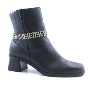 May include: Black leather ankle boot with a square toe and a block heel. A silver rhinestone band encircles the ankle. The boot has a side zipper and a low, chunky heel.