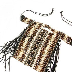 May include: A handcrafted necklace featuring a square pendant with a woven pattern of brown and cream-colored beads. The necklace has a fringed bottom and black leather straps. The necklace is designed with a unique, tribal aesthetic.