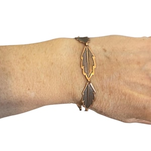 May include: A copper-toned bracelet featuring a series of stylized leaf-shaped links. The leaves have detailed veining and are connected by small, geometric links. The bracelet is worn on a wrist, showcasing its design and color.