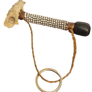 May include: A handcrafted key chain featuring a light-colored, textured handle with a carved design. The handle transitions to a section adorned with small white and black beads. A braided brown cord connects to a silver-colored key ring.