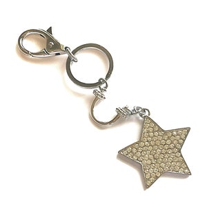 May include: A silver-toned keychain with a star-shaped charm. The star is encrusted with small, clear crystals. The keychain has a lobster clasp and a split ring for attaching keys.