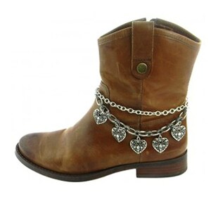 May include: A brown leather ankle boot with a silver chain ankle bracelet featuring heart-shaped charms. The boot has a worn appearance and a low heel. The chain is draped around the ankle, with the charms hanging down.