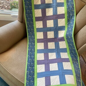 Può includere: Un runner da tavolo con sfondo bianco e un motivo di croci viola e blu. Il runner ha un bordo verde con un motivo di croci blu e bianche.