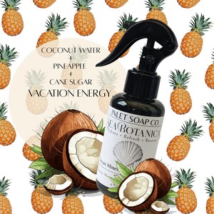 Może przedstawiać: Czarna butelka z rozpylaczem z napisem "INLET SOAP CO. SEA BOTANICA" i grafiką muszli. Obraz zawiera ilustracje kokosów, ananasów oraz słowa "COCONUT WATER + PINEAPPLE + CANE SUGAR VACATION ENERGY."
