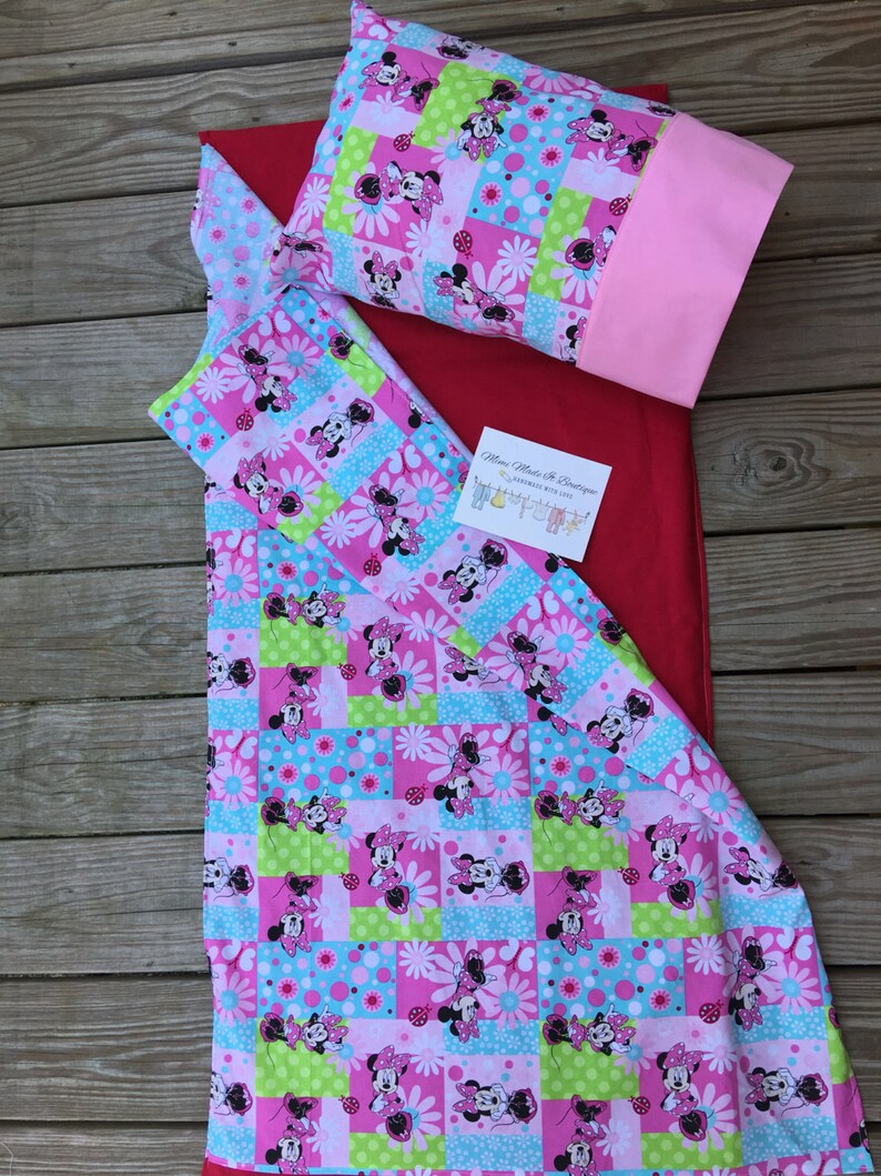 K&ouml;nnte beinhalten: Eine rot-wei&szlig;e Patchwork-Decke mit einem Minnie Mouse-Motiv. Die Decke besteht aus Quadraten aus verschiedenen Stoffen, die jeweils ein anderes Minnie Mouse-Muster aufweisen. Die Decke ist in der H&auml;lfte gefaltet und auf einer Holzoberfl&auml;che platziert.