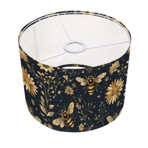 May include: A dark blue lampshade with a gold floral and bee pattern. The lampshade has a white interior and a white trim around the top.