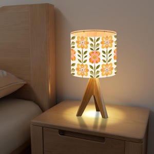 May include: A table lamp with a wooden base and a white lampshade with a floral pattern. The lampshade has orange, pink, and green flowers on a white background.