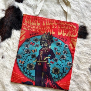 May include: Red tote bag with a graphic of a cat wearing a crown and a red dress. The bag has the text "Fare Thee Well Celebrating 50 Years of Grateful Dead 1965 - 2015" on the front.