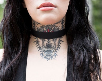 May include: A woman with long black hair wearing a black choker with a wolf tattoo on her neck.