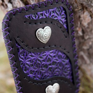 May include: A black leather wallet with a purple floral design and two silver heart-shaped accents.
