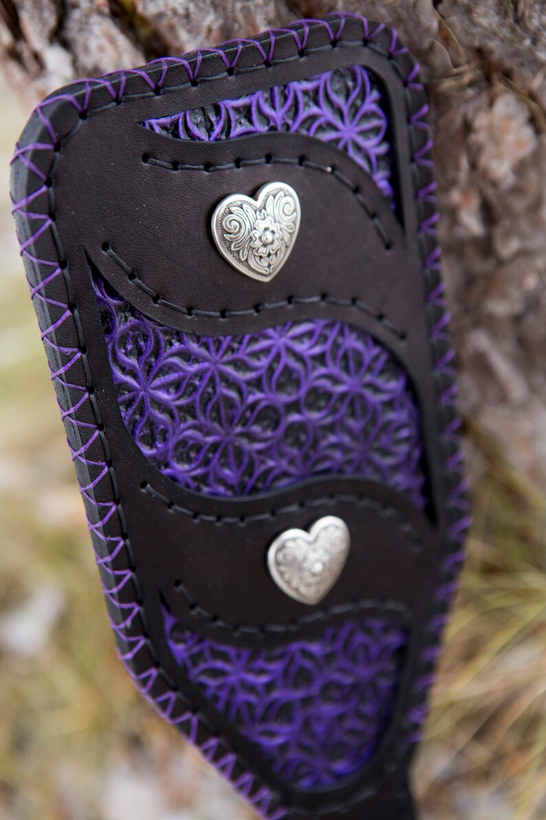 May include: A black leather wallet with a purple floral design and two silver heart-shaped accents.