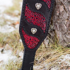 May include: A black leather paddle with red and black floral detailing and three silver heart-shaped accents.