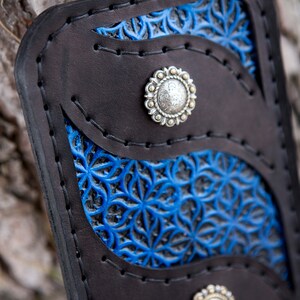May include: A black leather wallet with blue floral embossed details and silver-toned metal accents. The wallet has three compartments and a snap closure.