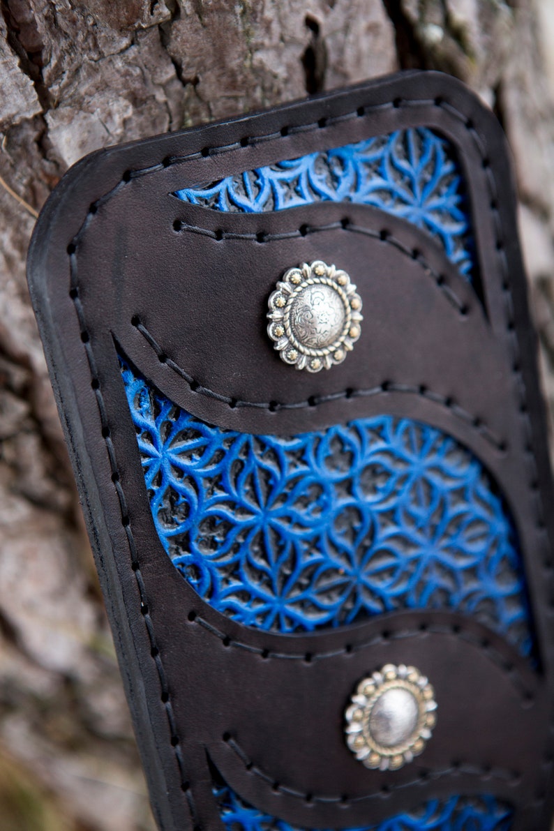 May include: A black leather wallet with blue floral embossed details and silver-toned metal accents. The wallet has three compartments and a snap closure.