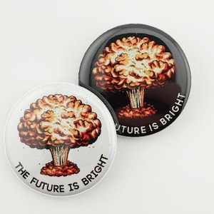 May include: Two round button pins with a black and white background. The pins feature a cartoon image of a mushroom cloud with the text "The Future is Bright" on the white pin and "Future is Bright" on the black pin.