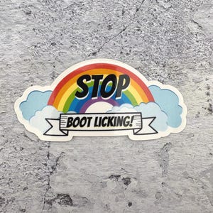 May include: A sticker with a rainbow design and the word "STOP" in bold black letters. Below the rainbow is a banner with the words "BOOT LICKING!". The sticker is surrounded by light blue clouds.