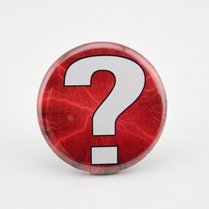 May include: A red button with a white question mark on it. The button has a textured surface.