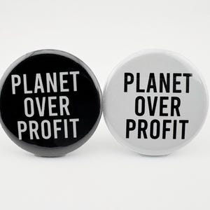 May include: Two round buttons with the text "Planet Over Profit" printed in white on a black button and a white button.