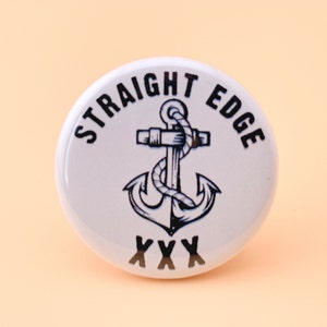 May include: White button with a black anchor and the text "STRAIGHT EDGE" above the anchor and "XXX" below the anchor.