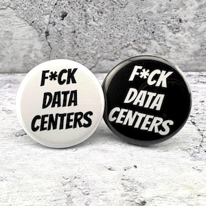 May include: Two circular pin-back buttons, one white with black text and one black with white text. Both buttons feature the phrase F*CK DATA CENTERS in a bold, sans-serif font. The buttons are round with a smooth, glossy finish and a metal backing.