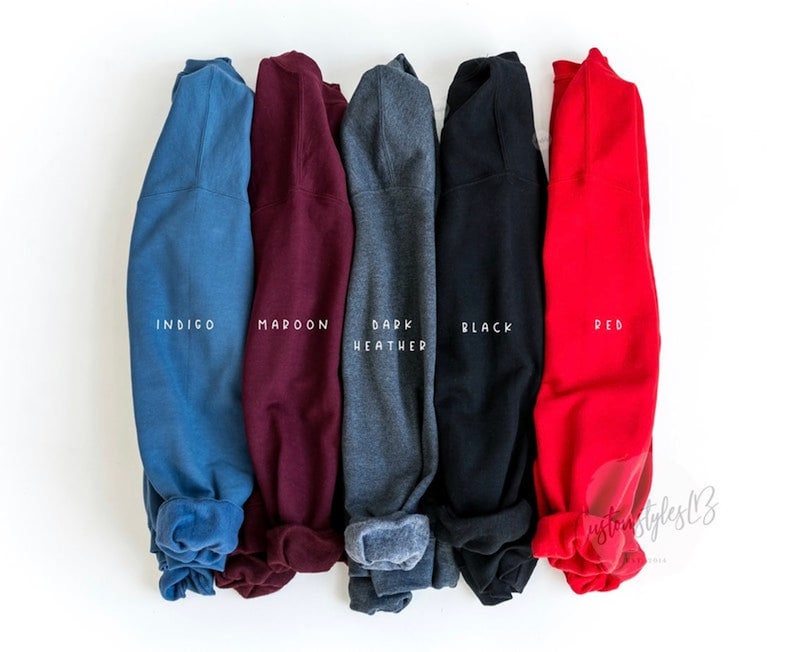 May include: Five folded sweatshirts in different colours: indigo, maroon, dark heather, black, and red. Each sweatshirt has the colour name printed on the cuff.