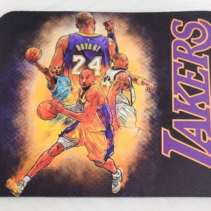 May include: A black mousepad with a purple and orange "LAKERS" logo and a graphic of four basketball players in Lakers uniforms. The players are wearing jerseys with the numbers 24, 3, and 8. One player is holding a basketball.