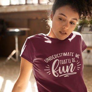 Puede incluir: Una camiseta color granate con un gr&aacute;fico blanco que dice "Underestimate me that'll be fun".