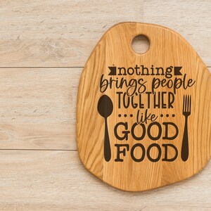 K&ouml;nnte beinhalten: Ein Schneidebrett aus Holz mit einem Griff und dem eingravierten Text "nothing brings people together like good food". Ein L&ouml;ffel und eine Gabel sind ebenfalls auf das Brett graviert.