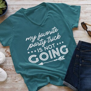 Puede incluir: Camiseta de cuello en V azul turquesa con el texto "my favorite party trick... is not going" en letras blancas con una flecha blanca apuntando hacia la derecha.