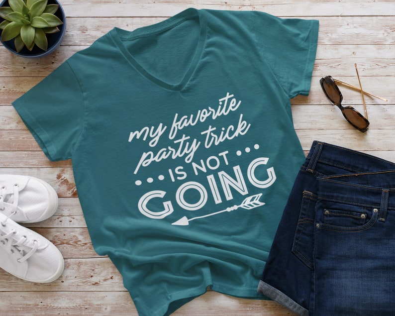 Puede incluir: Camiseta de cuello en V azul turquesa con el texto "my favorite party trick... is not going" en letras blancas con una flecha blanca apuntando hacia la derecha.