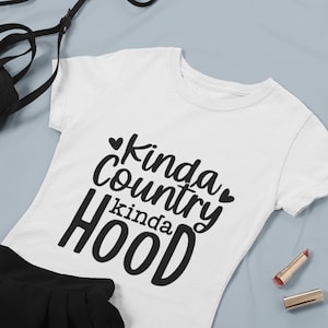 May include: White t-shirt with black text that reads "Kinda Country Kinda Hood" with a heart symbol on either side of the word "Country".