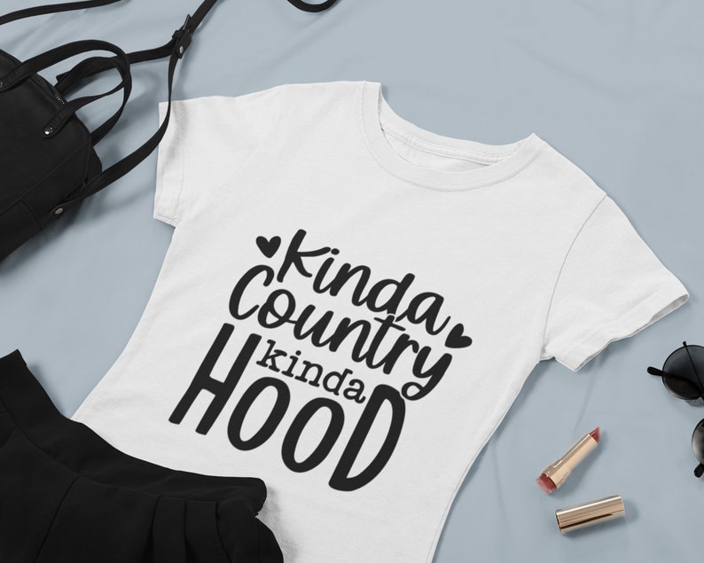 May include: White t-shirt with black text that reads "Kinda Country Kinda Hood" with a heart symbol on either side of the word "Country".