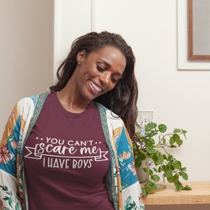 Pode incluir: Uma camiseta vinho com o texto "...YOU CAN'T... scare me I HAVE BOYS" impresso em branco na frente. A camiseta est&aacute; sendo usada por uma pessoa com cabelo comprido e escuro.