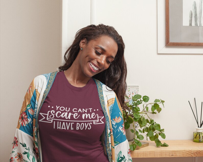 Pode incluir: Uma camiseta vinho com o texto "...YOU CAN'T... scare me I HAVE BOYS" impresso em branco na frente. A camiseta est&aacute; sendo usada por uma pessoa com cabelo comprido e escuro.