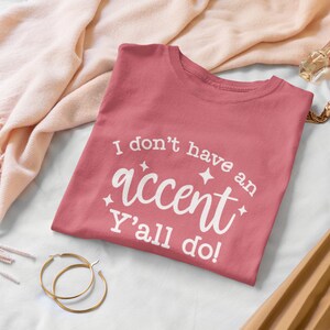 May include: A pink t-shirt with the text "I don't have an accent Y'all do!" in white lettering.