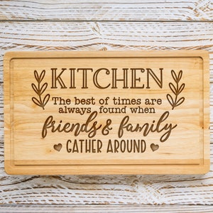 K&ouml;nnte beinhalten: Ein Schneidebrett aus Holz mit dem eingravierten Text "KITCHEN The best of times are always found when friends & family GATHER AROUND".