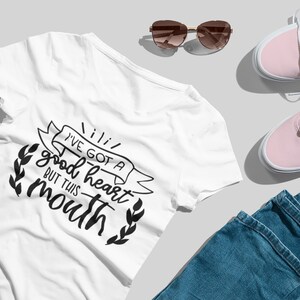 Puede incluir: Camiseta blanca con un gr&aacute;fico negro que dice "Tengo un buen coraz&oacute;n pero esta boca". El gr&aacute;fico est&aacute; rodeado de una pancarta y hojas.