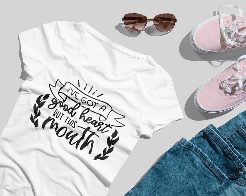 Puede incluir: Camiseta blanca con un gr&aacute;fico negro que dice "Tengo un buen coraz&oacute;n pero esta boca". El gr&aacute;fico est&aacute; rodeado de una pancarta y hojas.